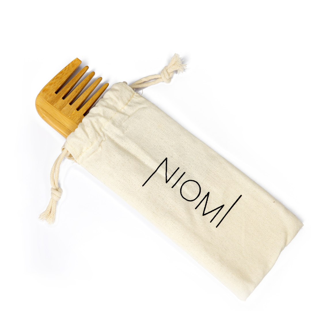A bamboo detangling comb with the brand name 'NIOMI' inscribed on the flat edge. In a NIOMI bag