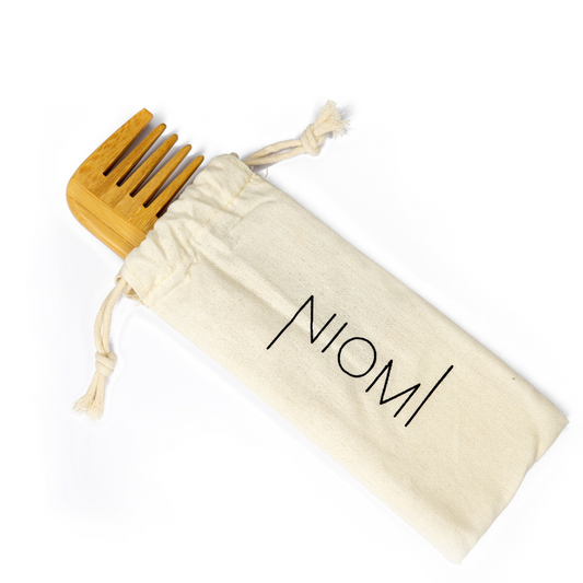 A bamboo detangling comb with the brand name 'NIOMI' inscribed on the flat edge. In a NIOMI bag