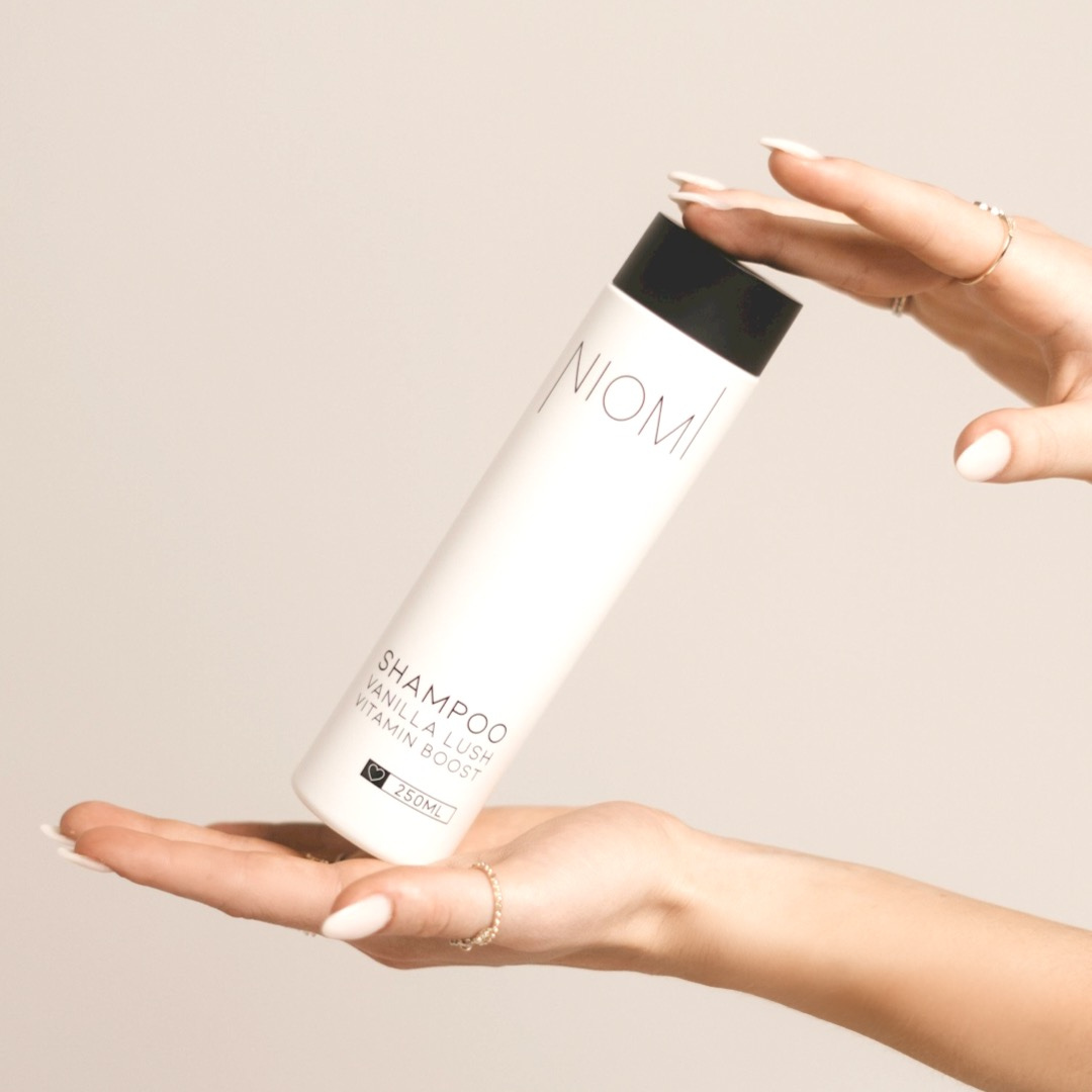 A bottle of NIOMI Vanilla Lush, Vitamin Boost Shampoo 250ml with a white label and black cap.

