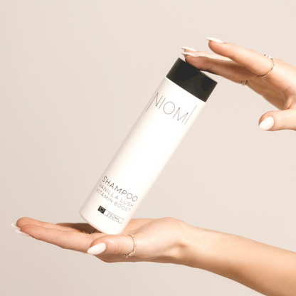 A bottle of NIOMI Vanilla Lush, Vitamin Boost Shampoo 250ml with a white label and black cap.

