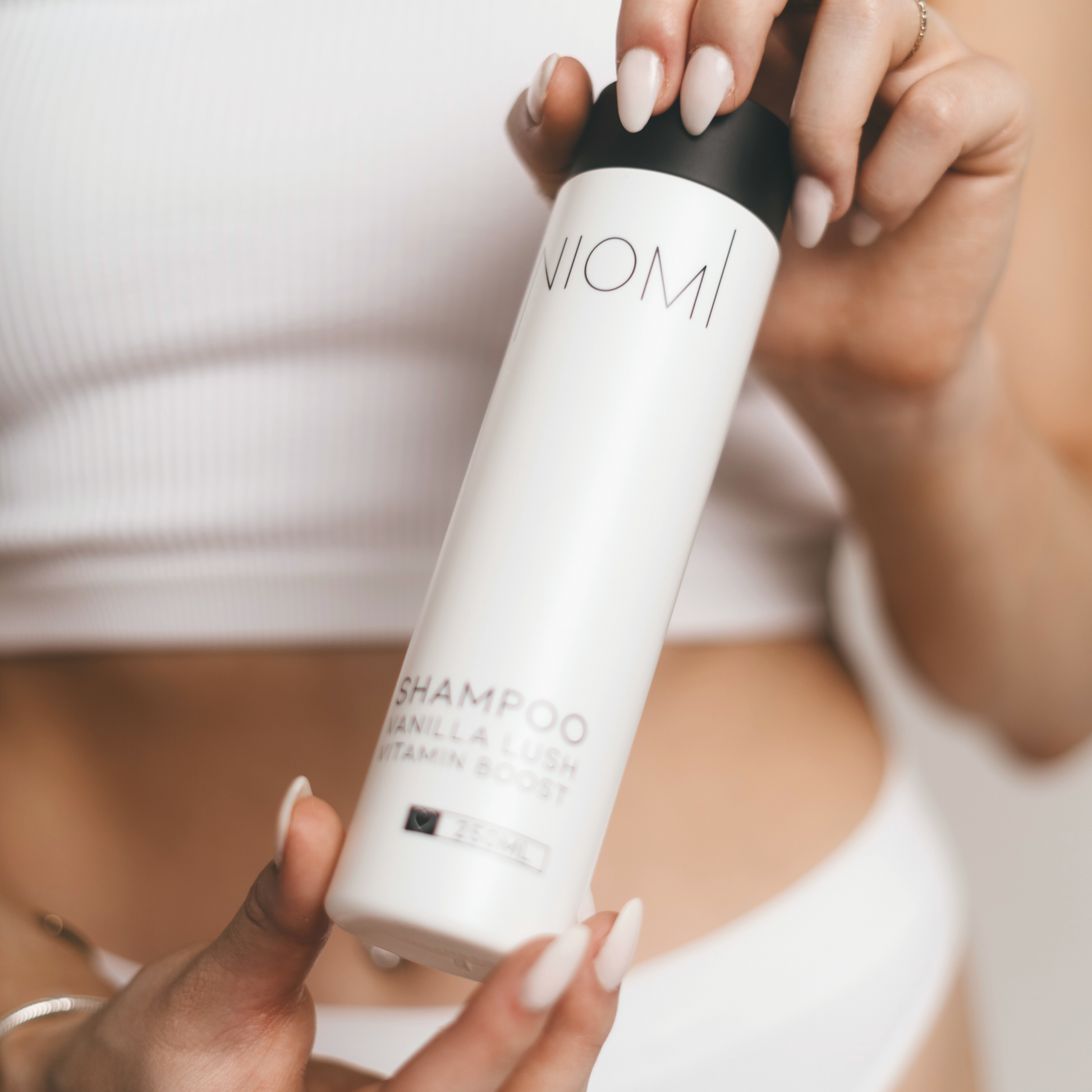 A bottle of NIOMI Vanilla Lush, Vitamin Boost Shampoo 250ml with a white label and black cap.

