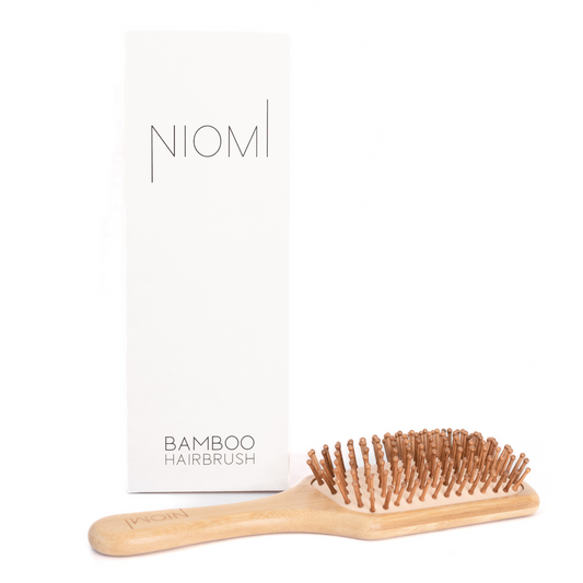A NIOMI Bamboo Paddle Hairbrush with a wooden handle and bamboo bristles, placed next to its packaging box.